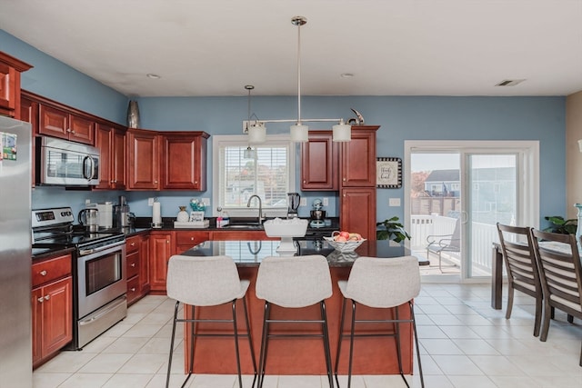 kitchen featuring stainless steel appliances, dark stone counters, a center island, sink, and pendant lighting