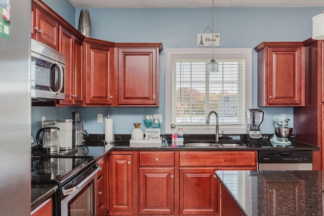 kitchen featuring stainless steel appliances, hanging light fixtures, sink, and dark stone countertops