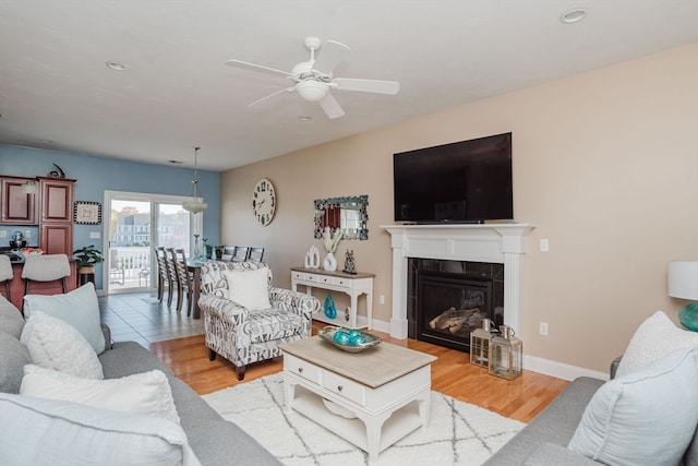 living room with a tiled fireplace, light hardwood / wood-style floors, and ceiling fan