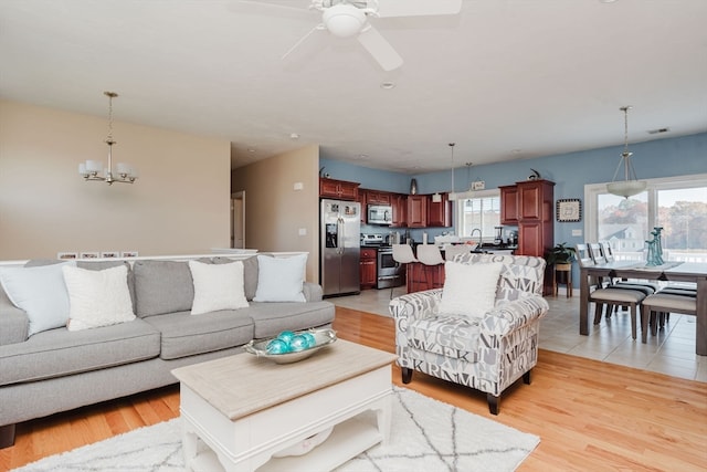 living room with light hardwood / wood-style floors and ceiling fan with notable chandelier