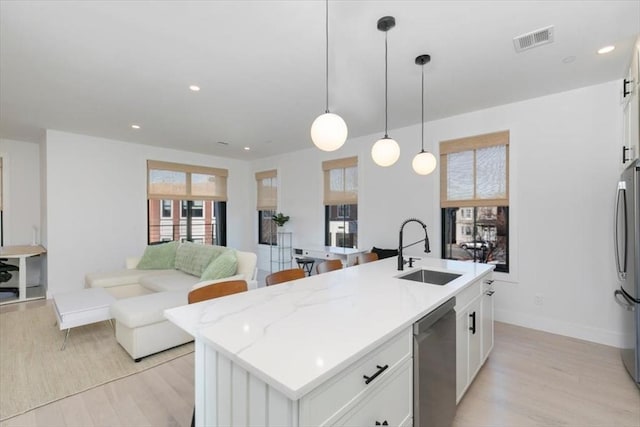 kitchen featuring appliances with stainless steel finishes, white cabinetry, sink, hanging light fixtures, and a center island with sink