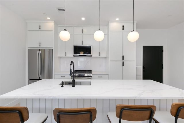 kitchen featuring decorative backsplash, hanging light fixtures, stainless steel appliances, and an island with sink