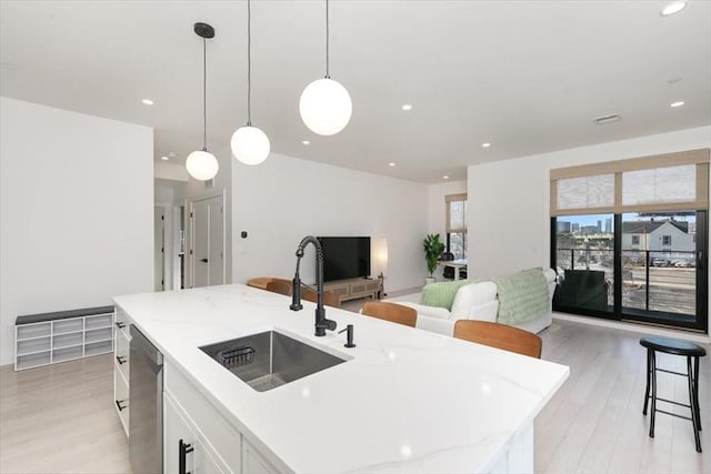 kitchen with a center island with sink, pendant lighting, stainless steel dishwasher, white cabinets, and sink