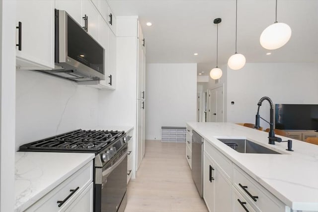 kitchen featuring light stone countertops, white cabinets, appliances with stainless steel finishes, sink, and hanging light fixtures