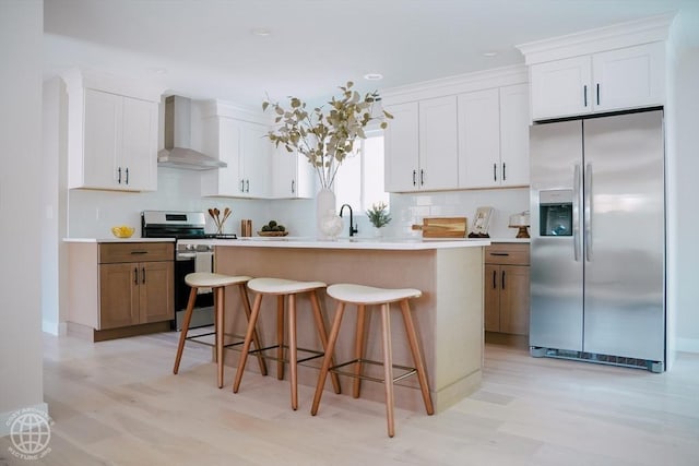 kitchen featuring appliances with stainless steel finishes, wall chimney range hood, light wood-style floors, backsplash, and recessed lighting