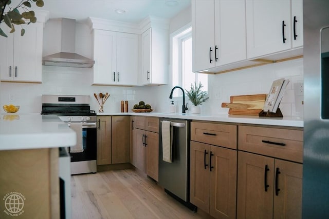 kitchen with wall chimney range hood, stainless steel appliances, light wood-style floors, light countertops, and recessed lighting