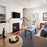 living area with stairs, wood finished floors, and a warm lit fireplace