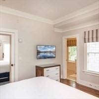 bedroom featuring baseboards, ensuite bathroom, crown molding, and wood finished floors