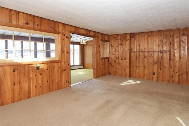 spare room with a chandelier, carpet floors, baseboard heating, and wooden walls