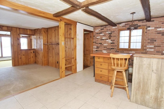 unfurnished office featuring beamed ceiling, a healthy amount of sunlight, light colored carpet, and wooden walls