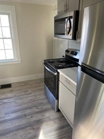 kitchen with white cabinetry, appliances with stainless steel finishes, backsplash, and light hardwood / wood-style floors