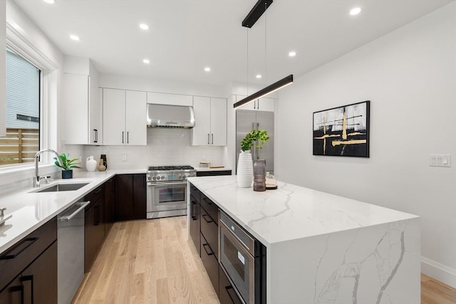 kitchen featuring a sink, a center island, wall chimney exhaust hood, white cabinets, and built in appliances