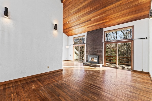 unfurnished living room with a fireplace, a towering ceiling, hardwood / wood-style flooring, and wooden ceiling