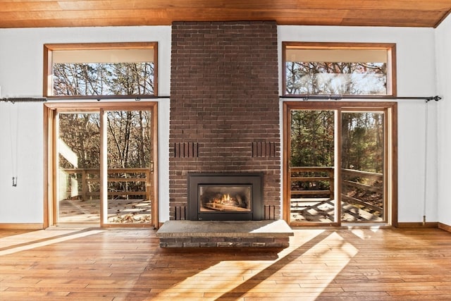 unfurnished living room with a brick fireplace, light hardwood / wood-style flooring, a wealth of natural light, and wooden ceiling