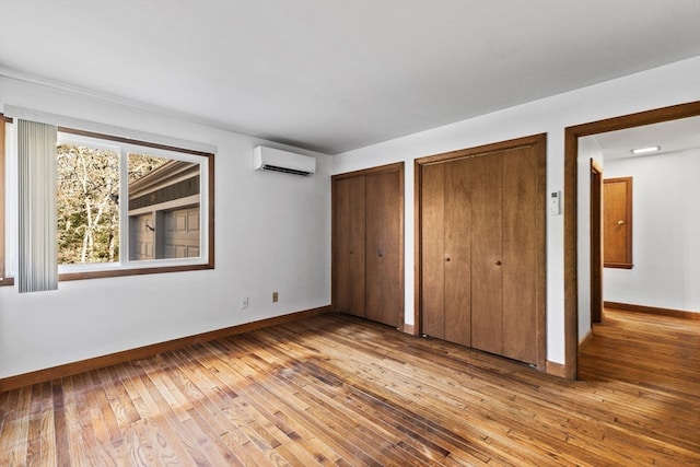 unfurnished bedroom featuring light hardwood / wood-style flooring, a wall mounted air conditioner, and two closets