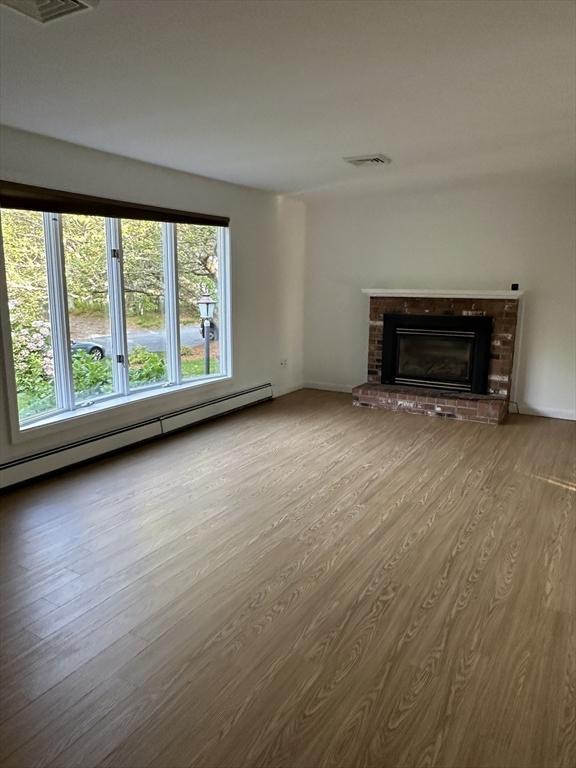 21 Friends Ln, Dennis, MA 02660 - unfurnished living room with wood finished floors, a brick fireplace, and a baseboard heating unit