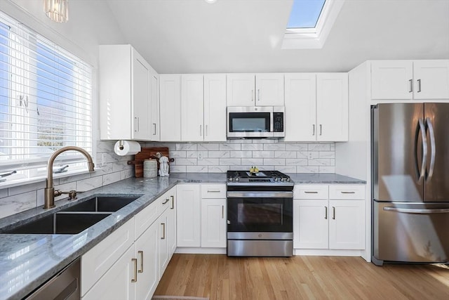 kitchen featuring lofted ceiling with skylight, stone counters, stainless steel appliances, and a sink