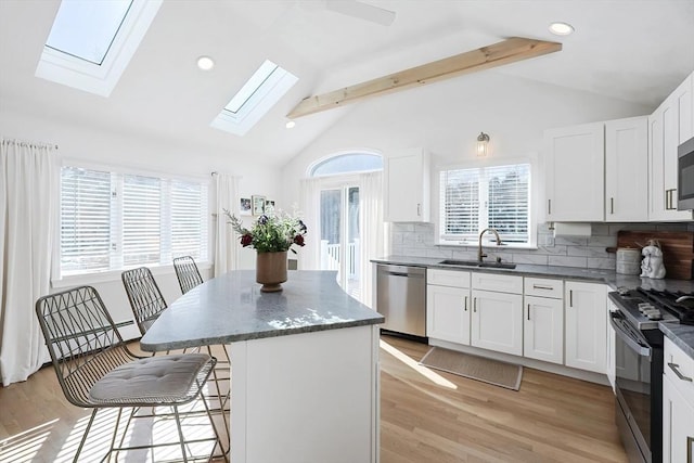 kitchen featuring a center island, stainless steel appliances, lofted ceiling with skylight, a sink, and a kitchen breakfast bar