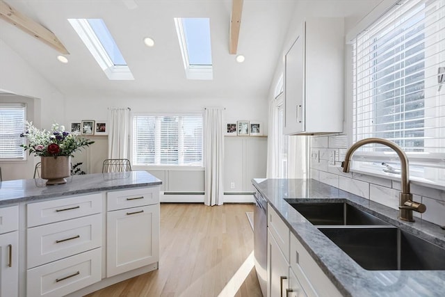 kitchen featuring vaulted ceiling with skylight, plenty of natural light, a sink, and white cabinetry