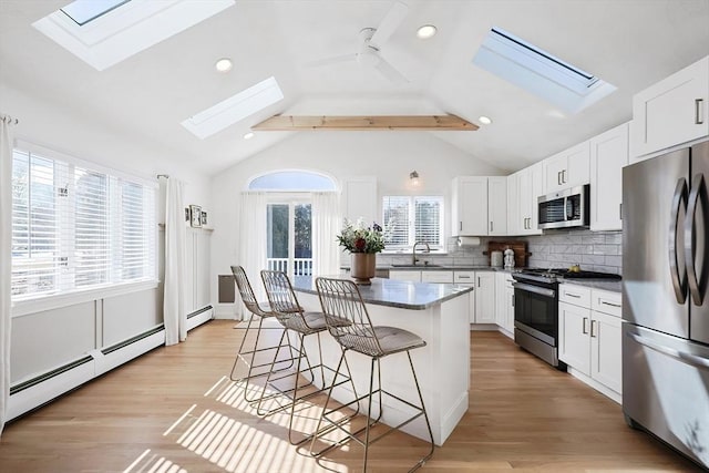 kitchen featuring dark countertops, a kitchen breakfast bar, baseboard heating, stainless steel appliances, and a sink