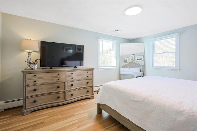 bedroom featuring a baseboard heating unit, light wood-type flooring, and visible vents