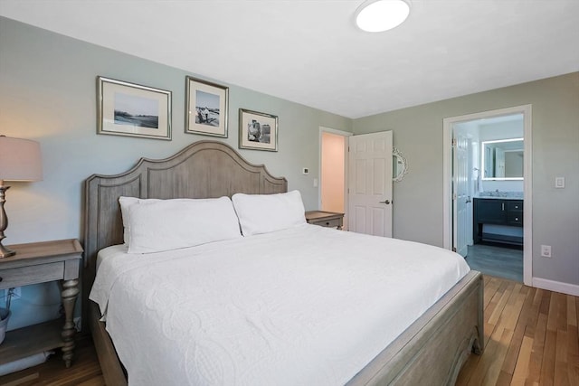 bedroom with baseboards, a sink, wood finished floors, and connected bathroom