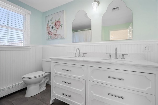 full bathroom featuring visible vents, wainscoting, toilet, a baseboard heating unit, and a sink