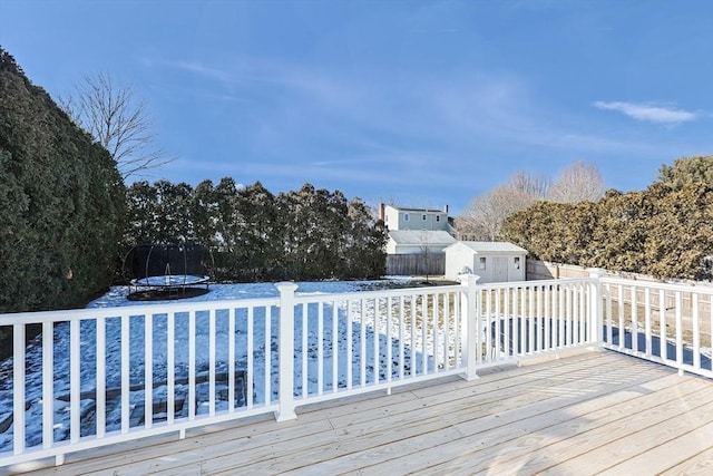 wooden deck with a trampoline, an outdoor structure, fence, and a shed