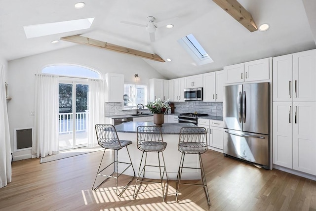 kitchen featuring dark countertops, lofted ceiling with skylight, appliances with stainless steel finishes, a breakfast bar, and white cabinetry