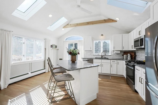 kitchen with stainless steel appliances, a baseboard radiator, light wood-style floors, white cabinets, and a kitchen breakfast bar