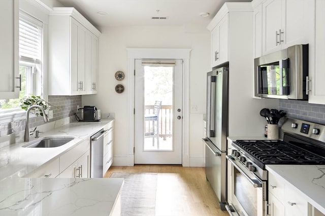 kitchen featuring sink, white cabinets, light stone counters, light hardwood / wood-style floors, and stainless steel appliances