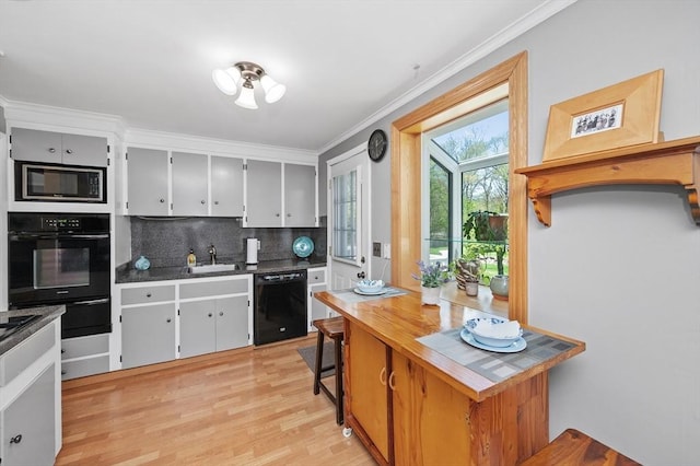 kitchen with crown molding, tasteful backsplash, light wood-type flooring, a sink, and black appliances