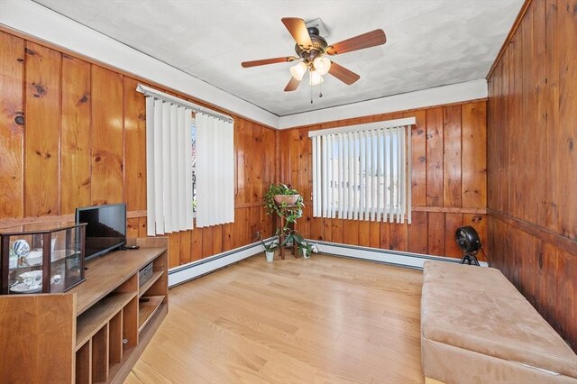 unfurnished room with wooden walls, baseboard heating, ceiling fan, and wood finished floors