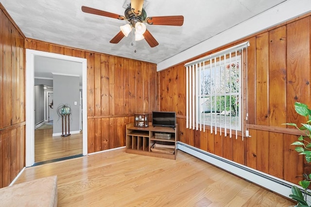 living room featuring wood finished floors, baseboards, ceiling fan, wooden walls, and a baseboard heating unit