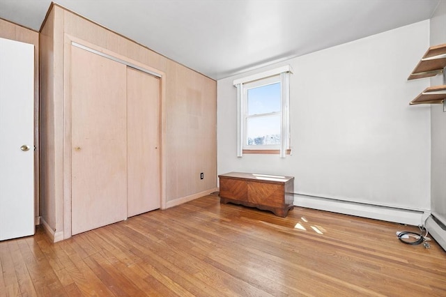 unfurnished bedroom featuring baseboard heating, hardwood / wood-style flooring, and a closet