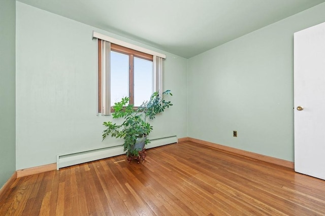 spare room featuring baseboards, a baseboard heating unit, and hardwood / wood-style flooring