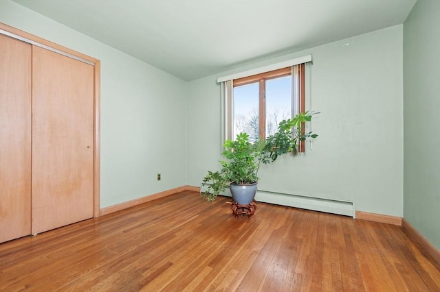 unfurnished bedroom with baseboards, light wood-style flooring, a baseboard heating unit, and a closet