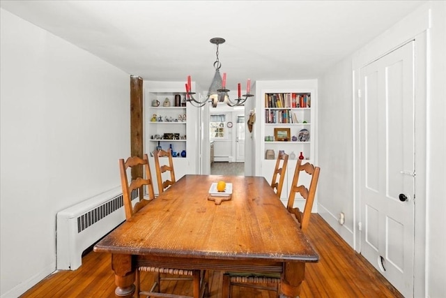 dining area with built in shelves, a notable chandelier, radiator, baseboard heating, and wood finished floors