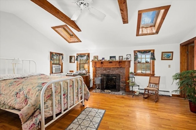 bedroom featuring a baseboard heating unit, vaulted ceiling with skylight, a brick fireplace, and wood finished floors