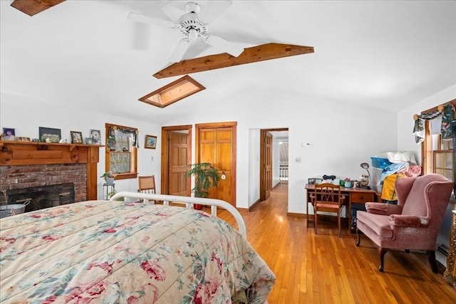 bedroom with vaulted ceiling with beams, light wood-style flooring, a ceiling fan, baseboards, and a brick fireplace