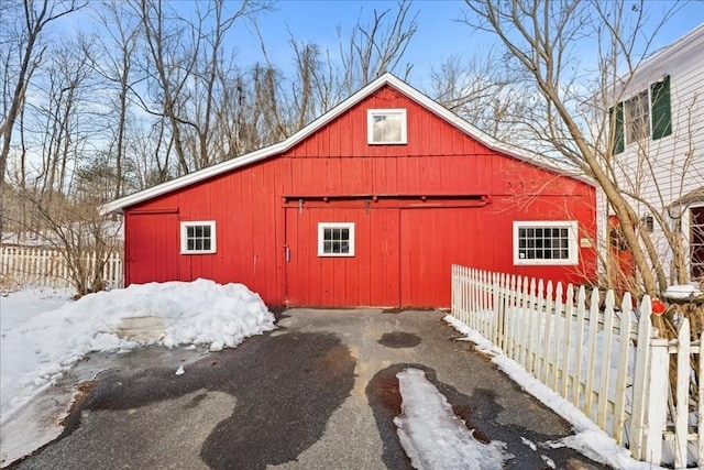 snow covered structure featuring an outbuilding, a barn, and fence