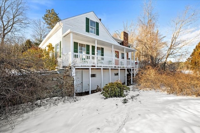 snow covered house with covered porch and a chimney