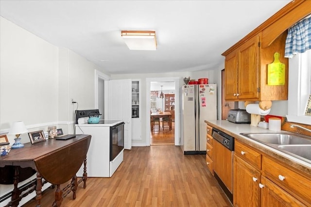 kitchen featuring light countertops, brown cabinetry, light wood-style floors, a sink, and white appliances