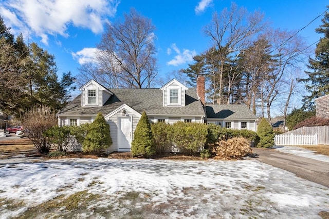 cape cod-style house featuring a chimney, fence, and roof with shingles