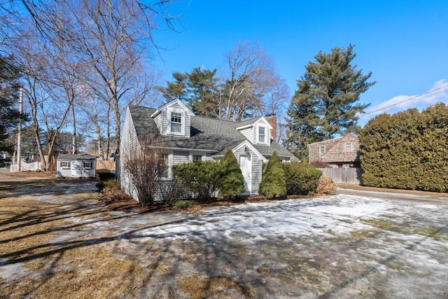 view of home's exterior featuring a storage shed, a shingled roof, an outbuilding, and fence