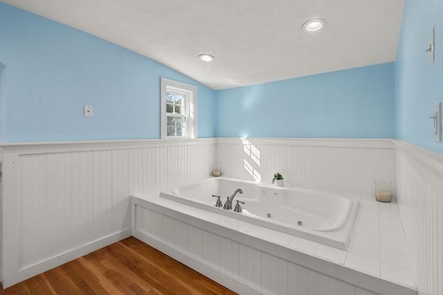 full bath featuring a wainscoted wall, vaulted ceiling, a whirlpool tub, and wood finished floors