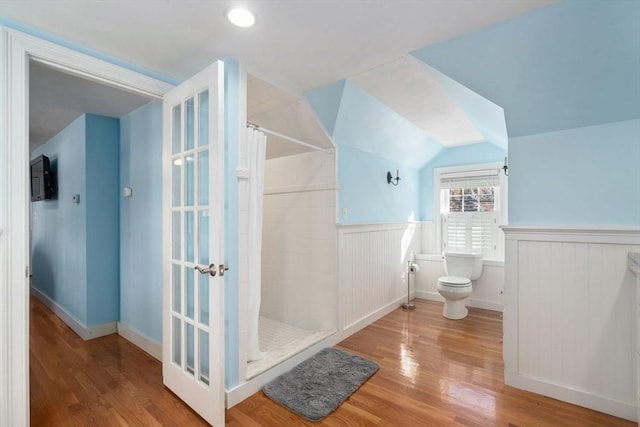 bathroom featuring wood finished floors, wainscoting, a tile shower, and toilet