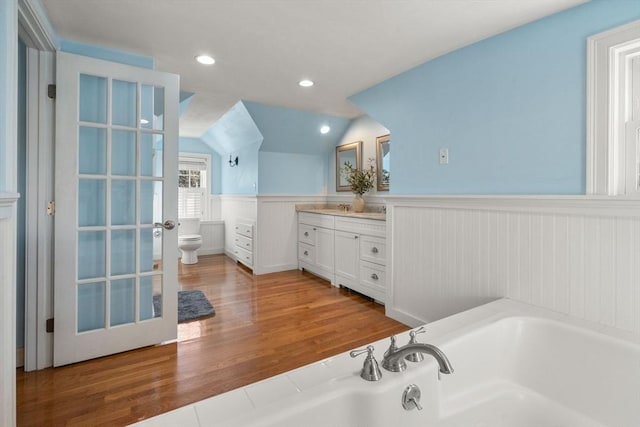 full bathroom with lofted ceiling, toilet, wainscoting, vanity, and a bath