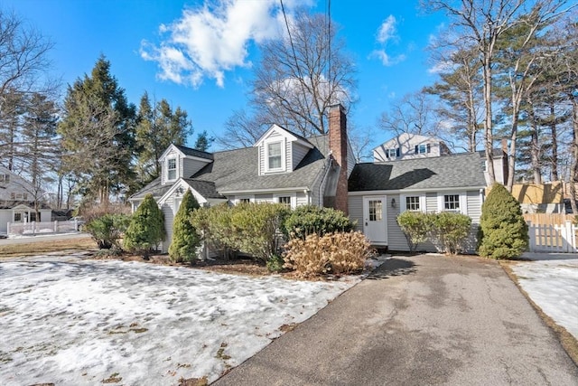 cape cod-style house with roof with shingles, a chimney, and fence