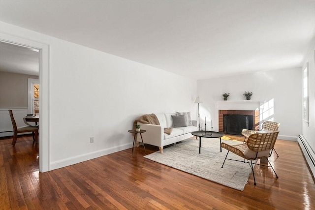 living room with a brick fireplace, wood-type flooring, baseboards, and a baseboard heating unit